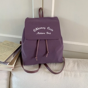 Macro view of purple nylon backpack with drawstring closure and white embroidery detail
