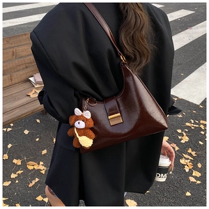 Deep brown glossy hobo bag with teddy bear pendant shown in an autumn street scene