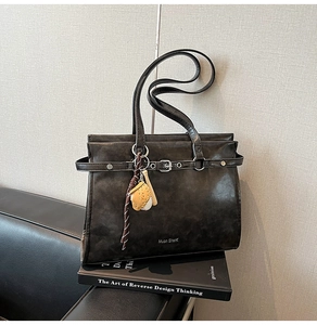 Detail of dark gray retro leather tote with baseball charm on a designer book