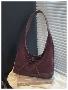 Close-up of vintage burgundy suede hobo bag with bow detail on white fabric