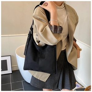 Detail of a black suede tote bag with front pocket and adjustable buckle strap on model