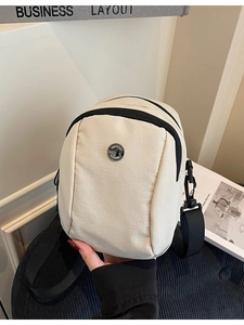 Minimalist off-white canvas crossbody bag with black strap and metallic circular logo