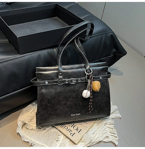 Detail of vintage black leather tote bag with metallic buckle and baseball glove charm