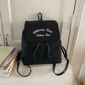 Close-up of black canvas backpack with white C&honey Cute Moborn embroidery and drawstrings