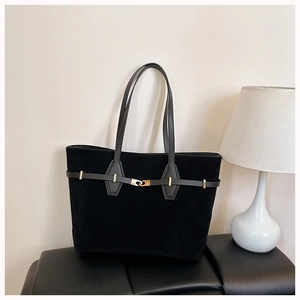 Close-up of black suede tote bag featuring a decorative gold buckle and leather handle