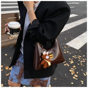 Detail view of dark brown faux leather shoulder bag with a cute plush bear charm accessory