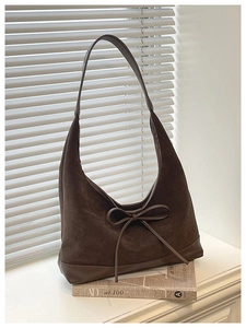 Detail of dark coffee suede hobo bag with bow on a book by white shutters
