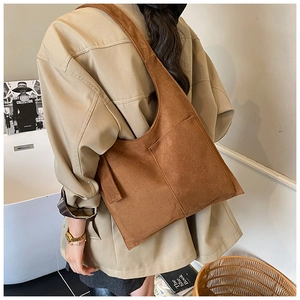 Close-up of a brown suede tote bag with a wide shoulder strap and large exterior pocket