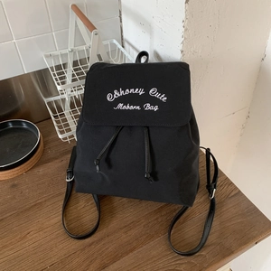 Detail of black canvas backpack showing white embroidery and drawstring flap closure