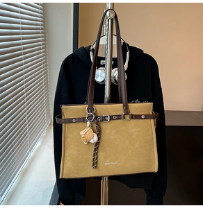 Detail of yellow suede tote bag with brown leather trim and baseball glove charm accessory