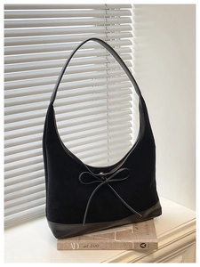 Detail view of black hobo bag featuring decorative bow and matte leather texture on window ledge