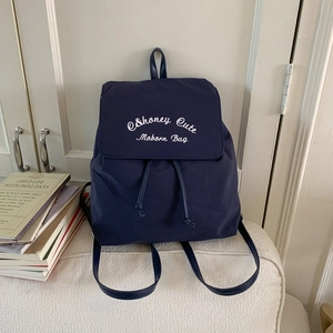 Detail view of navy blue nylon backpack with white embroidery and drawstring closure