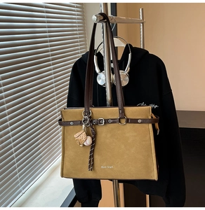 Detail of camel suede tote bag with dark brown leather straps and baseball glove charm