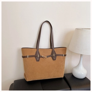 Detail of a large brown suede tote bag with leather strap and gold buckle on a black bench