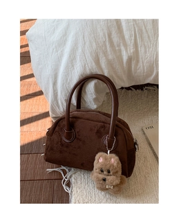 Nahaufnahme einer braunen Wildleder-Bowlingtasche mit Bärenanhänger auf einem Teppich