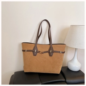Detail of a brown suede tote bag with leather handles and gold metal hardware