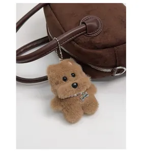 Detailansicht eines Plüsch-Hundeanhängers mit Perlenhalsband an einer Wildledertasche