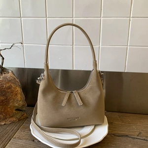 Detail view of khaki half-moon bag texture with dual zippers on a white tile backdrop