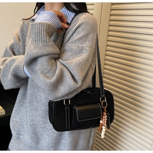 Detail of black vintage leather shoulder bag featuring white contrast stitching and beaded tassel