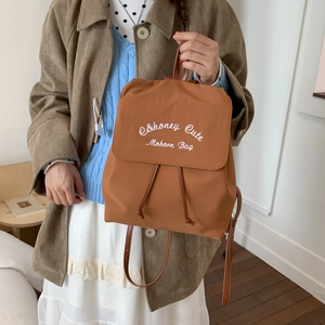 Detail of caramel nylon backpack featuring white embroidery and brown leather strap