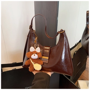 Detail of dark brown glossy underarm bag with cute plush bear charm and gold buckle