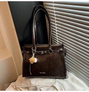 Detail of vintage brown tote bag with metal buckle and creative baseball pendant charm