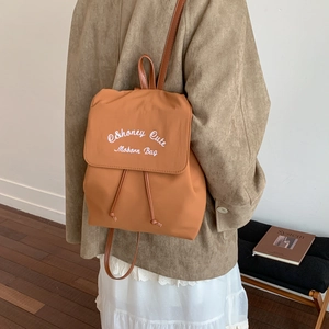 Detail of light brown nylon backpack with Honey Cute embroidery and leather strap