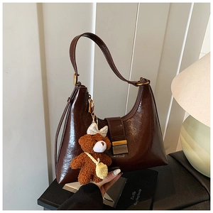 Detail of dark brown glossy leather hobo bag with gold buckle and plush bear charm