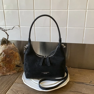 Detail of black semi-circle bag with silver logo and dual zippers on a styled display