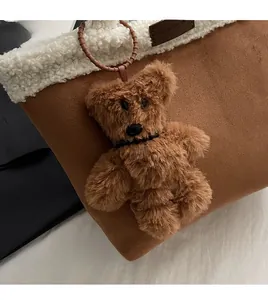 Close-up of a brown fluffy bear charm attached to a suede tote bag with stylish details