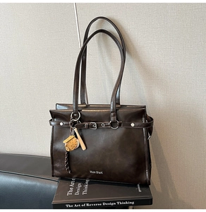 Detail of dark brown tote bag featuring silver buckle belt and baseball charm decor