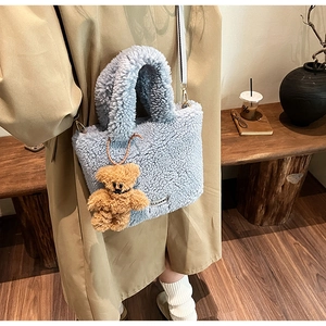 Detail of light blue fuzzy bucket bag with CLEAR label and brown teddy bear charm