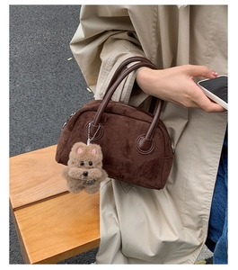 Detail of dark brown suede bowling bag with cute plush bear charm on a beige trench coat outfit