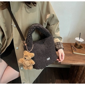 Detail of a brown plush crossbody bucket bag with bear pendant and clear logo