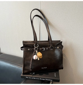 Detail of dark brown vintage tote bag with buckle strap and baseball glove charm