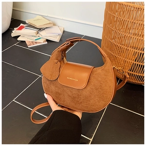 Detail of caramel suede half-moon bag featuring smooth leather flap and brand logo