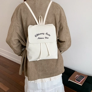 Detail view of cream backpack featuring drawstring closure and cute black embroidery