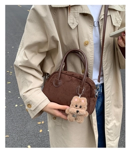 Detailed view of brown suede Boston bag featuring a plush puppy charm in outdoor setting