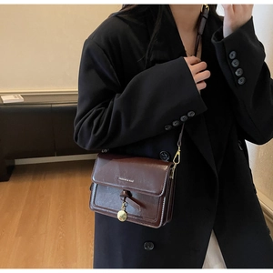 Détail du sac bandoulière vintage marron foncé avec nœud tissé et pendentif doré