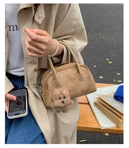 Detail der Wildleder-Handtasche mit Bärenanhänger und Perlenarmband auf dem Trenchcoat