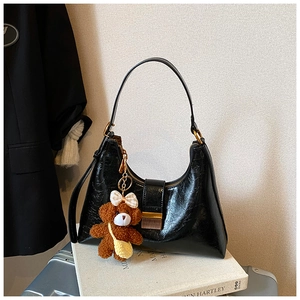 Close-up of black glossy leather crescent bag with gold hardware and a cute plush bear charm