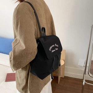 Detailed view of black canvas backpack featuring white embroidery and drawstring closure