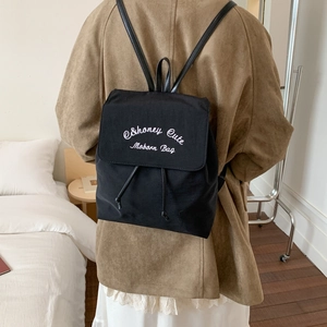 Close-up of black canvas backpack featuring elegant white script embroidery on the flap