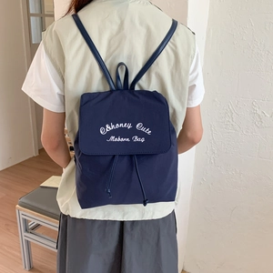 Detail view of navy blue backpack with drawstring closure and white embroidered lettering