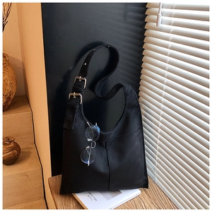 Close-up of black canvas tote bag with adjustable silver metal buckles on a wooden table