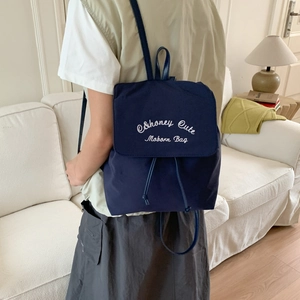 Detail of navy blue nylon backpack with white embroidery and leather straps in a home setting