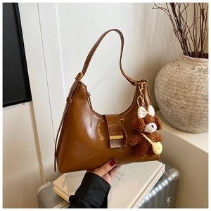 Detail of a brown crescent shoulder bag with glossy finish and a cute plush bear charm