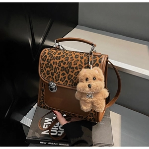 Détail du sac léopard avec boucle argentée et breloque chien en peluche sur livres