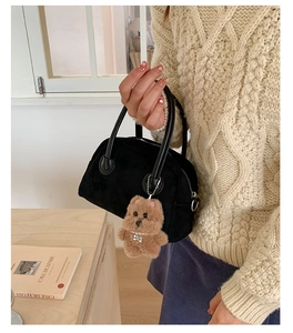 Detail of black faux suede handbag with a cute brown plush bear charm in a lifestyle setting