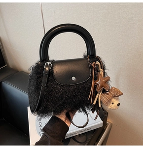 Detalle de bolso de peluche negro con asa de cuero y adorno de oso de peluche suave